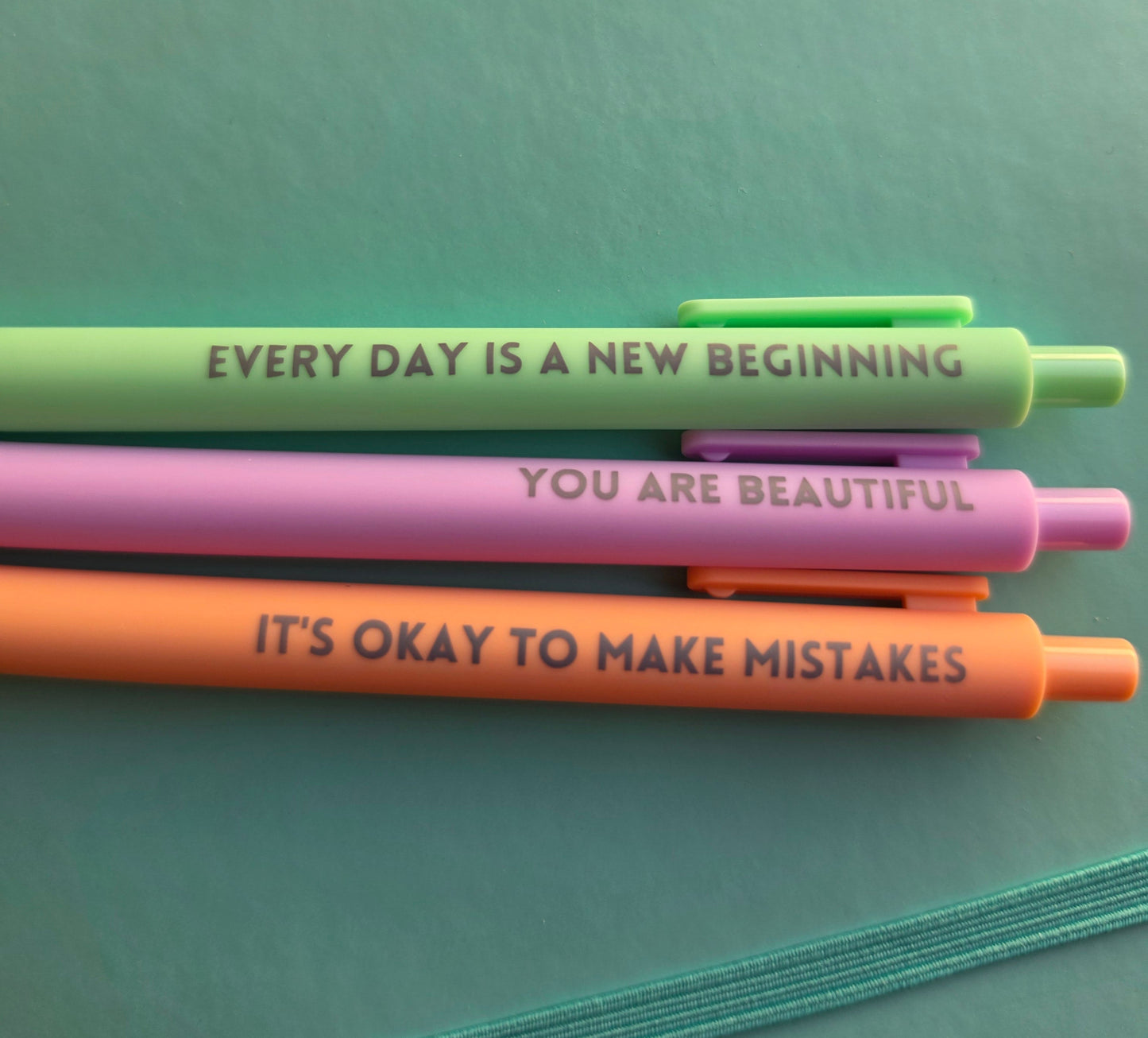 Three colorful pens with motivational quotes on a green surface
