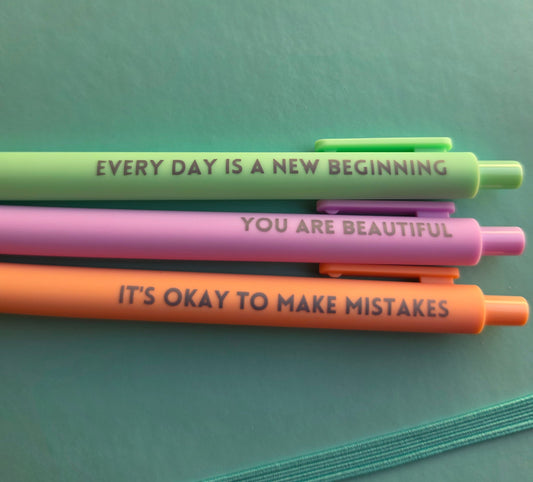 Three colorful pens with motivational quotes on a green surface