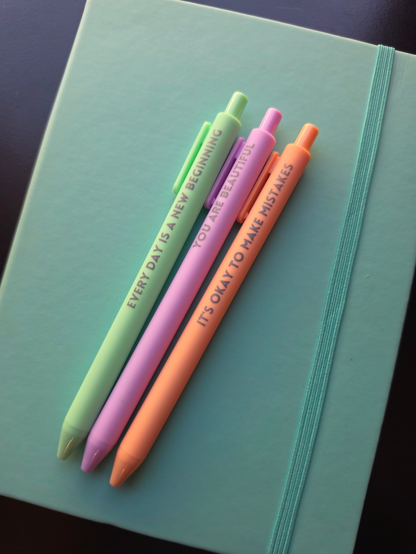 Four colorful pens with text on a teal surface