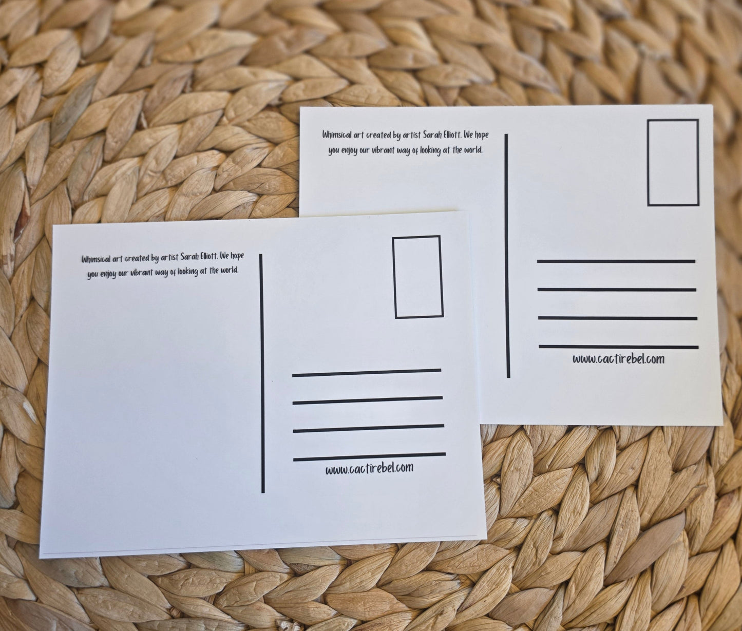 Two white postcards with printed lines and text are arranged on a round woven straw placemat over a dark surface.