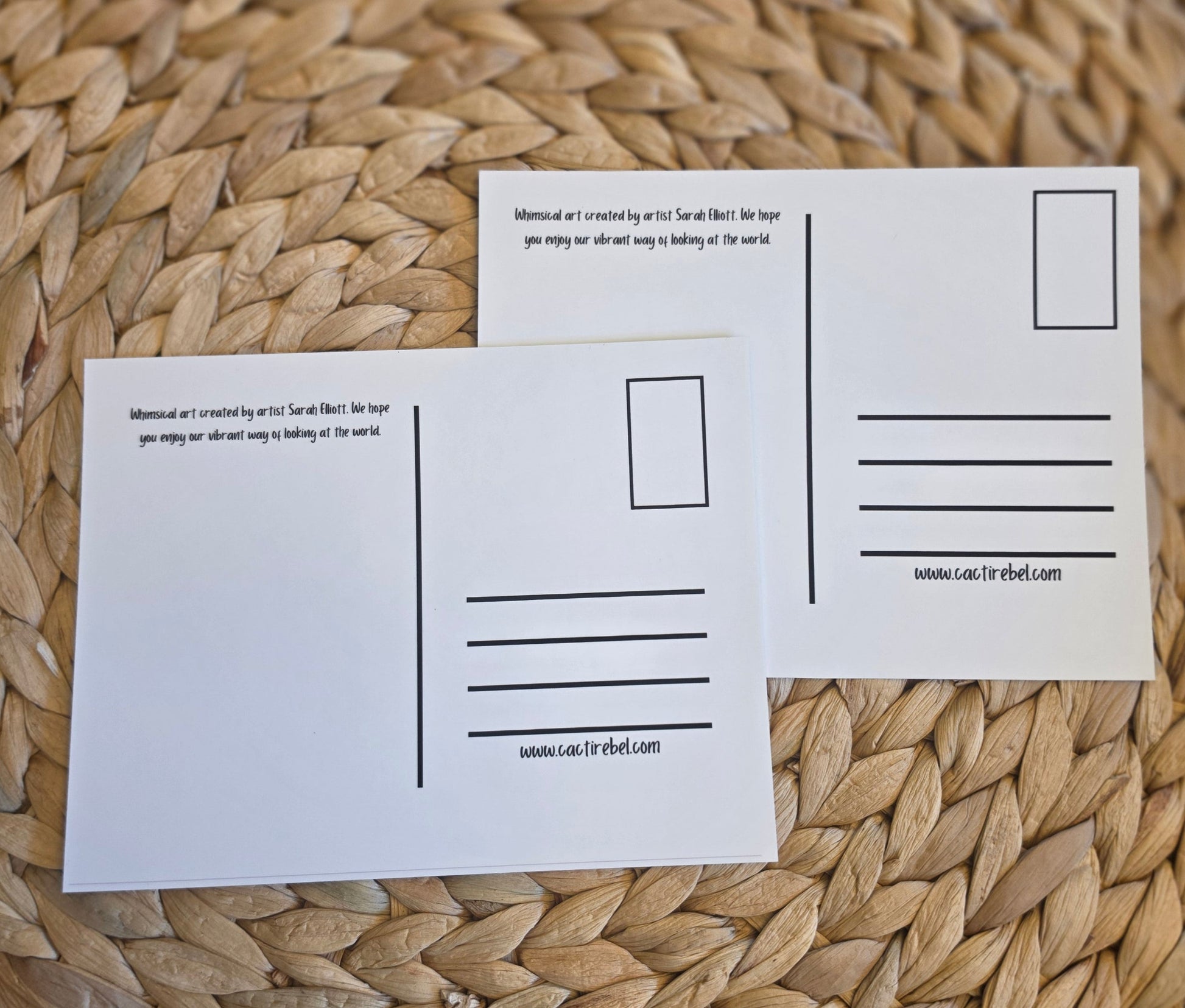 Two white postcards with printed lines and text are arranged on a round woven straw placemat over a dark surface.